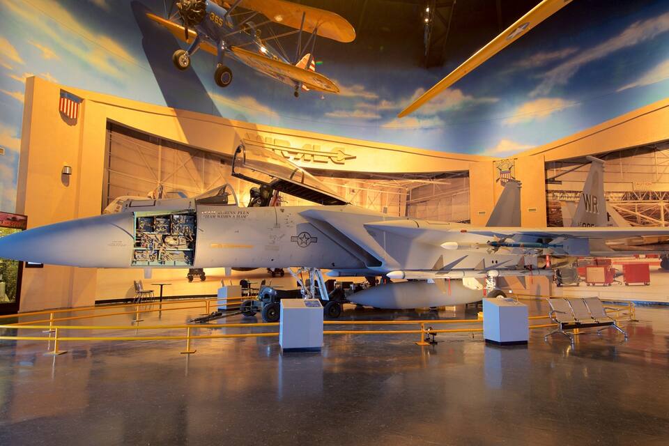 Un aereo da combattimento in un museo con un affresco raffigurante il cielo e altri modelli di aerei.