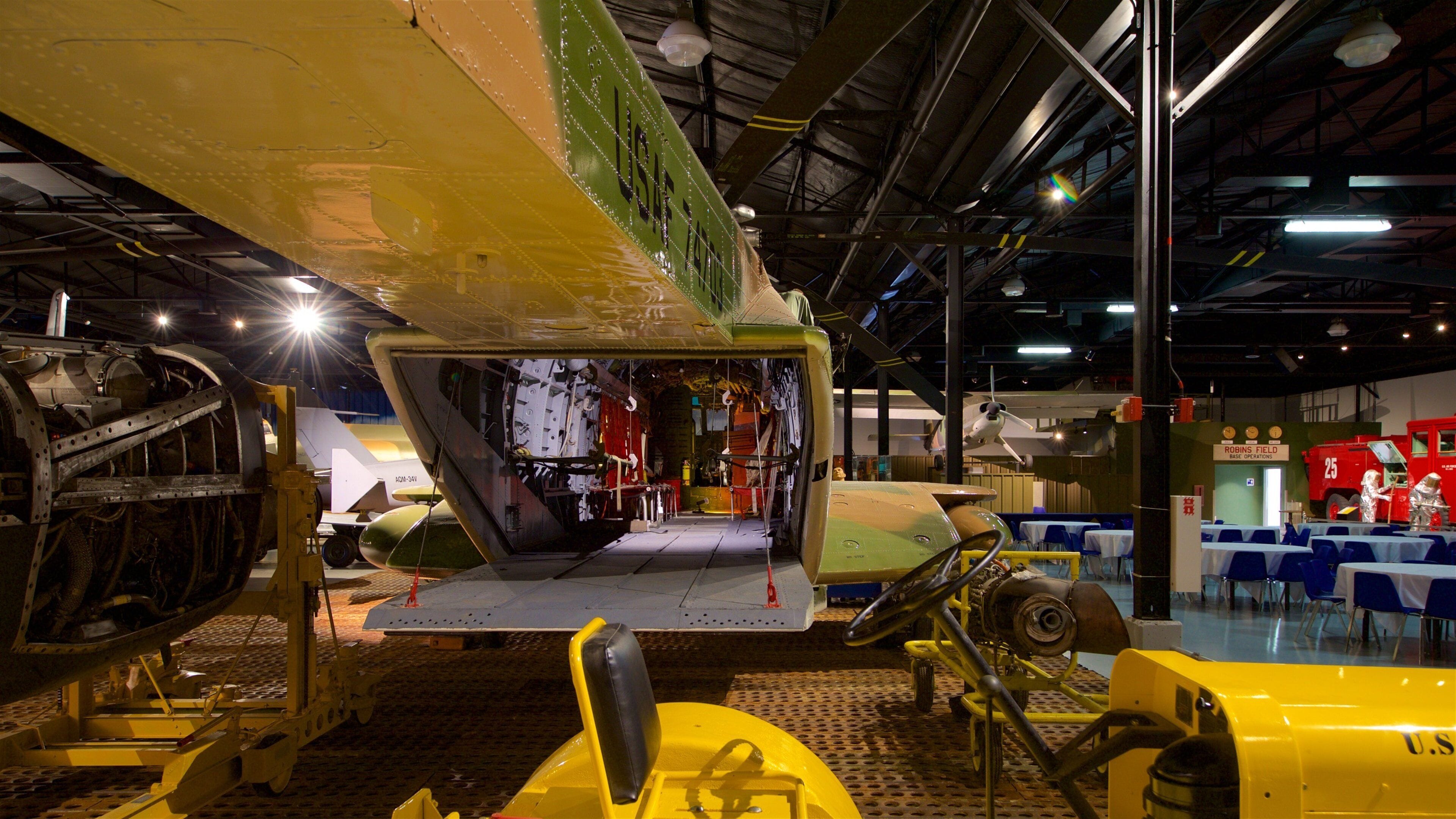 An aircraft fuselage with a green and yellow paint scheme, a yellow forklift, and a red fire truck in the background.