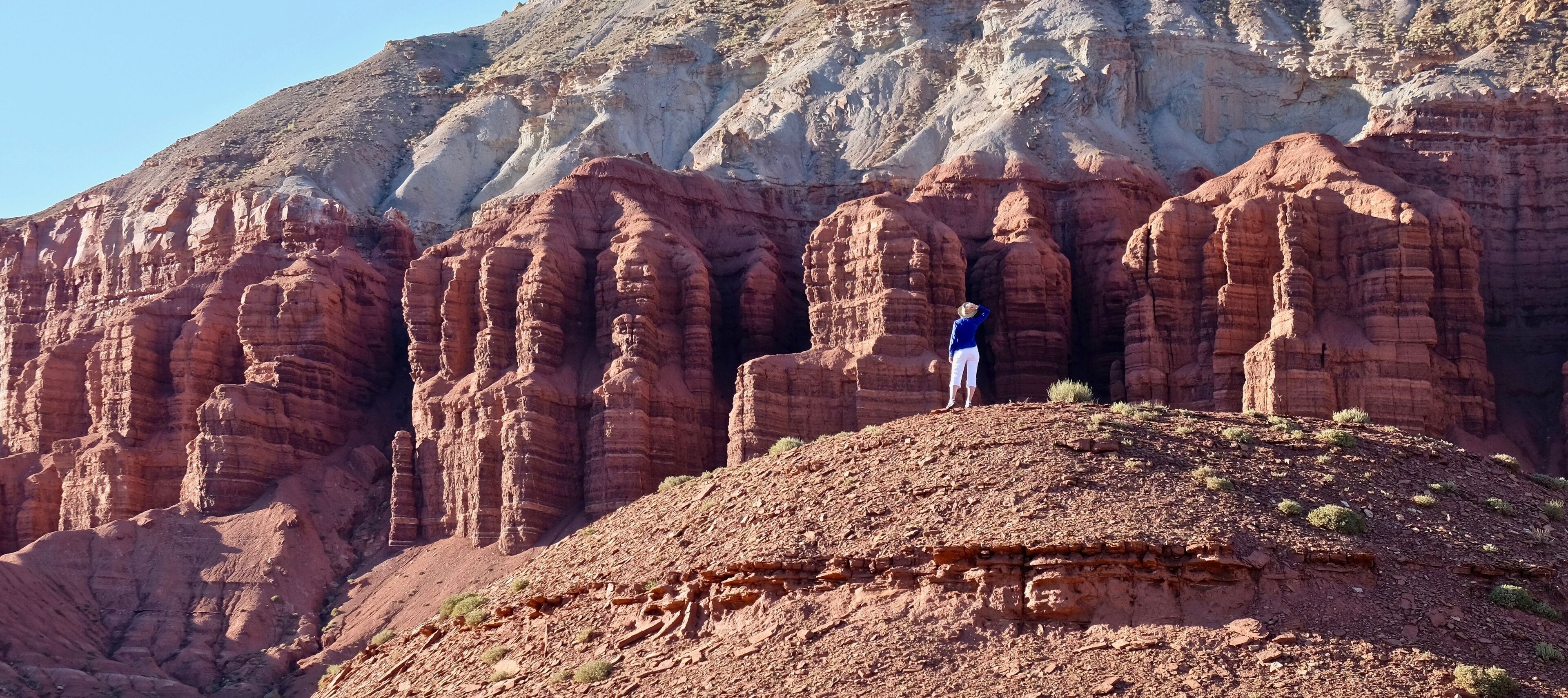 A person standing on a rocky hill with red rock formations in the background.