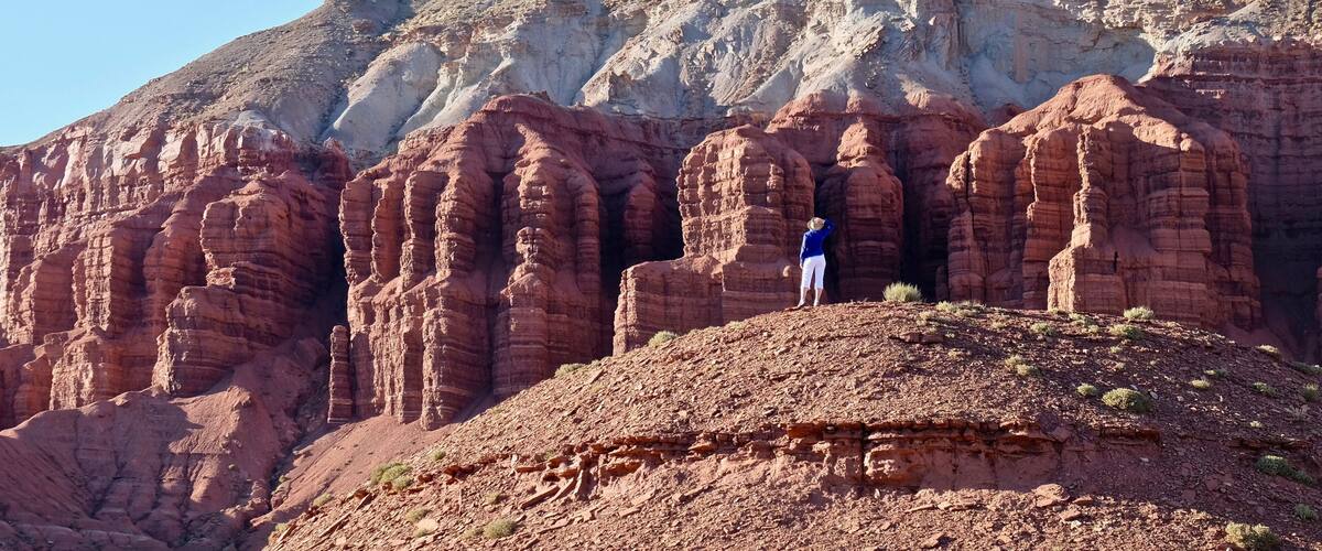 A person standing on a rocky hill with red rock formations in the background.