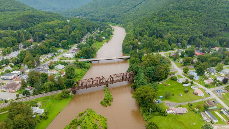 A river flowing through a valley with a bridge, surrounded by lush greenery and residential areas.