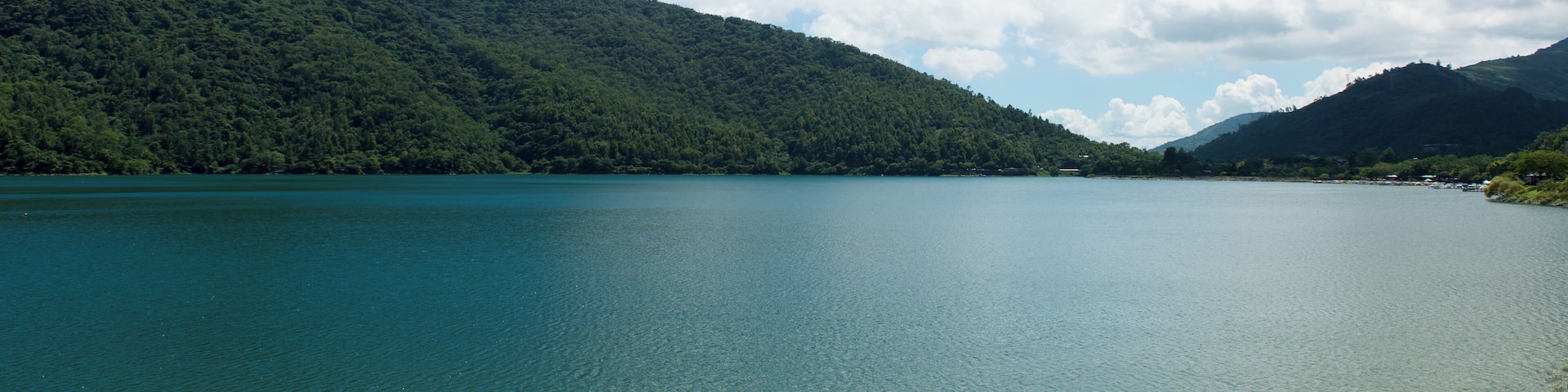 A calm lake surrounded by lush green hills under a partly cloudy sky.