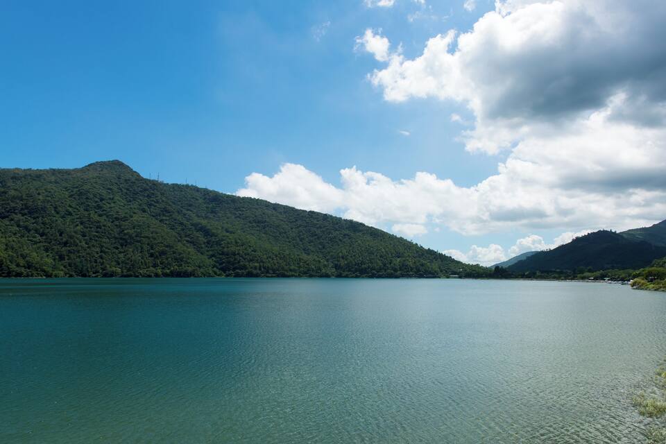 A calm lake surrounded by lush green hills under a partly cloudy sky.