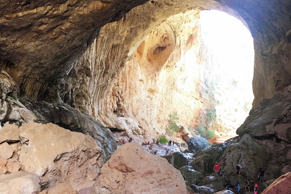 Una cueva con un arco natural, terreno rocoso y un arroyo.