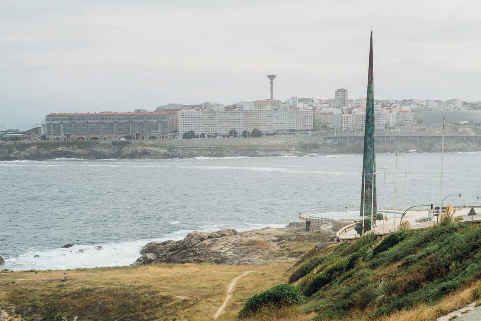 A coastal cityscape with a prominent tower, a promenade, and rocky terrain.