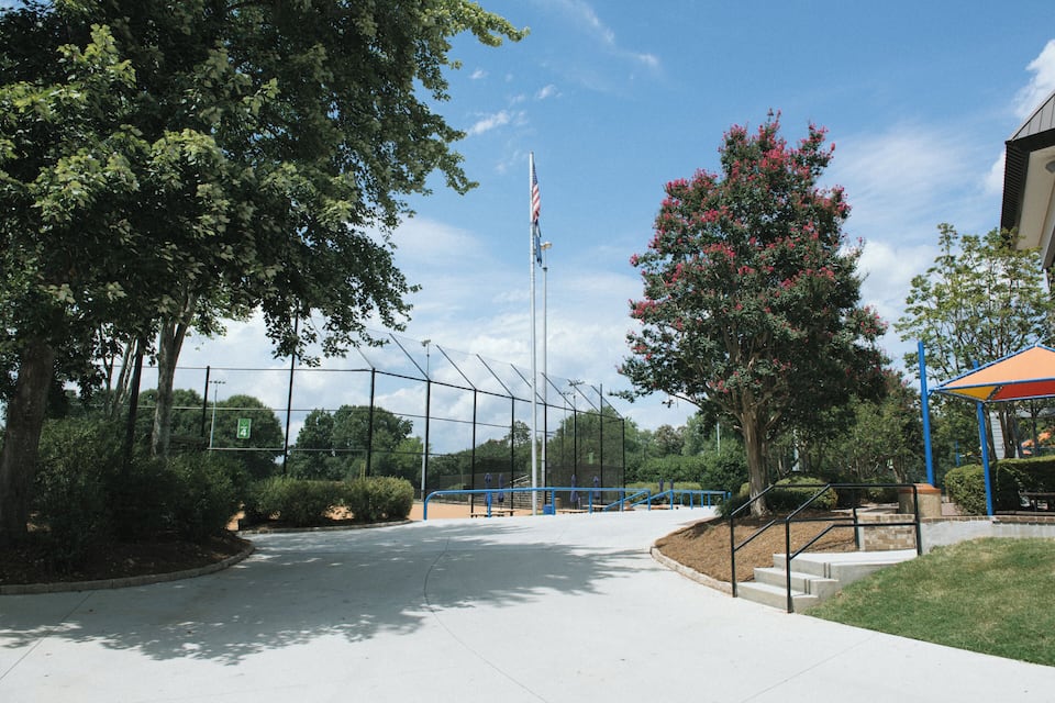 A sports field with a flagpole, trees, and a pavilion.