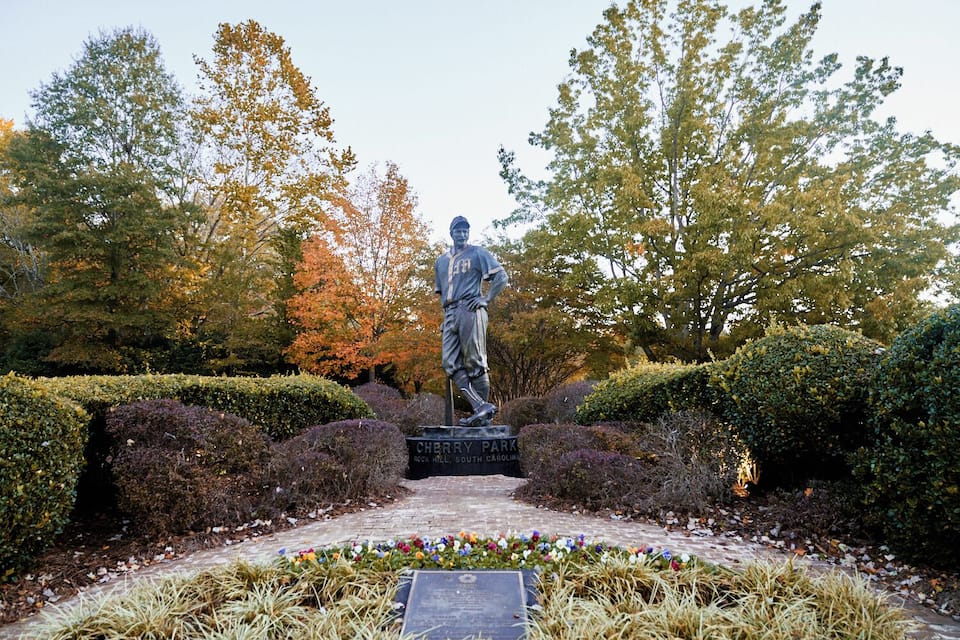 A statue in a park with neatly trimmed hedges and colorful flowers.
