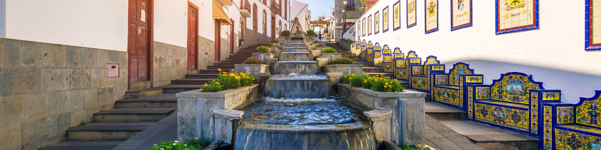 A narrow street with a water feature in the center, flanked by buildings with balconies and tiled walls.