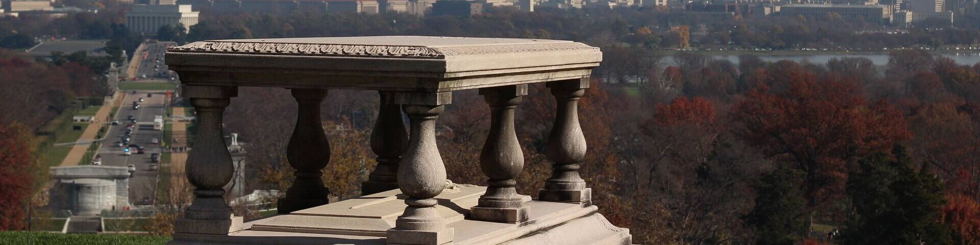 Una barandilla de piedra con columnas que da a una vista panorámica de la ciudad, con un obelisco destacado en la distancia.