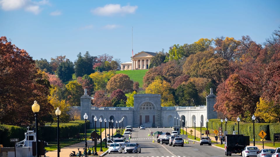 A road leading to a large white building with columns, surrounded by autumn-colored trees.