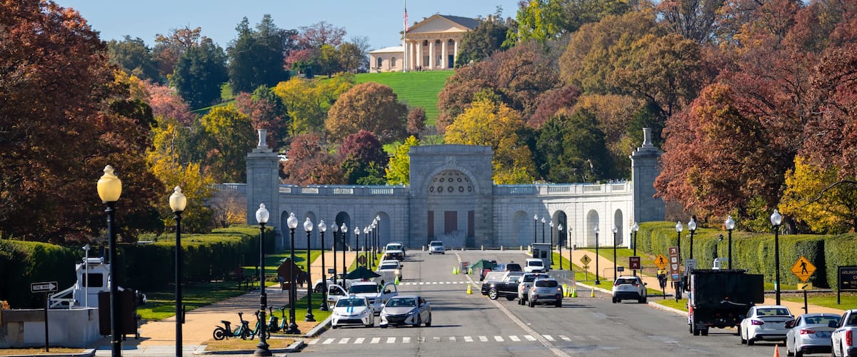 A road leading to a large white building with columns, surrounded by autumn-colored trees.