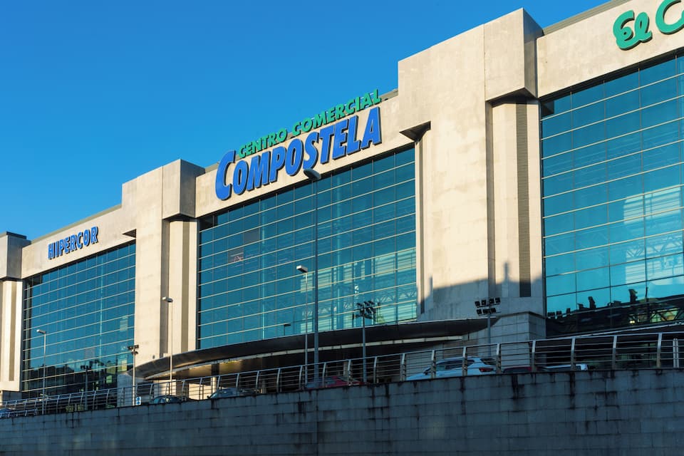 Un edificio comercial con amplios ventanales de vidrio y letrero que dice 'COMPOSTELA'.