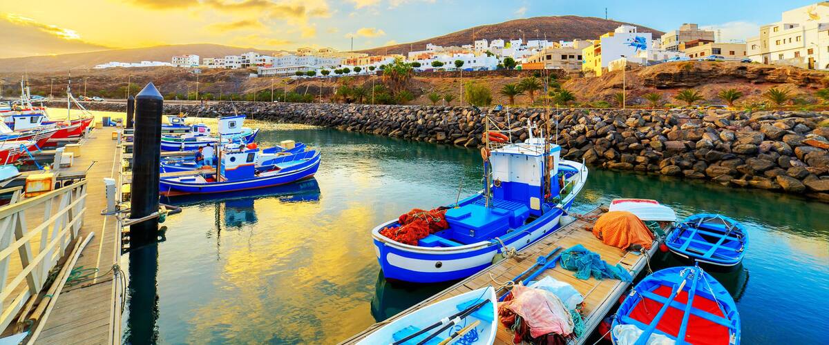 A harbor with boats docked, a rocky shoreline, and white buildings in the background.
