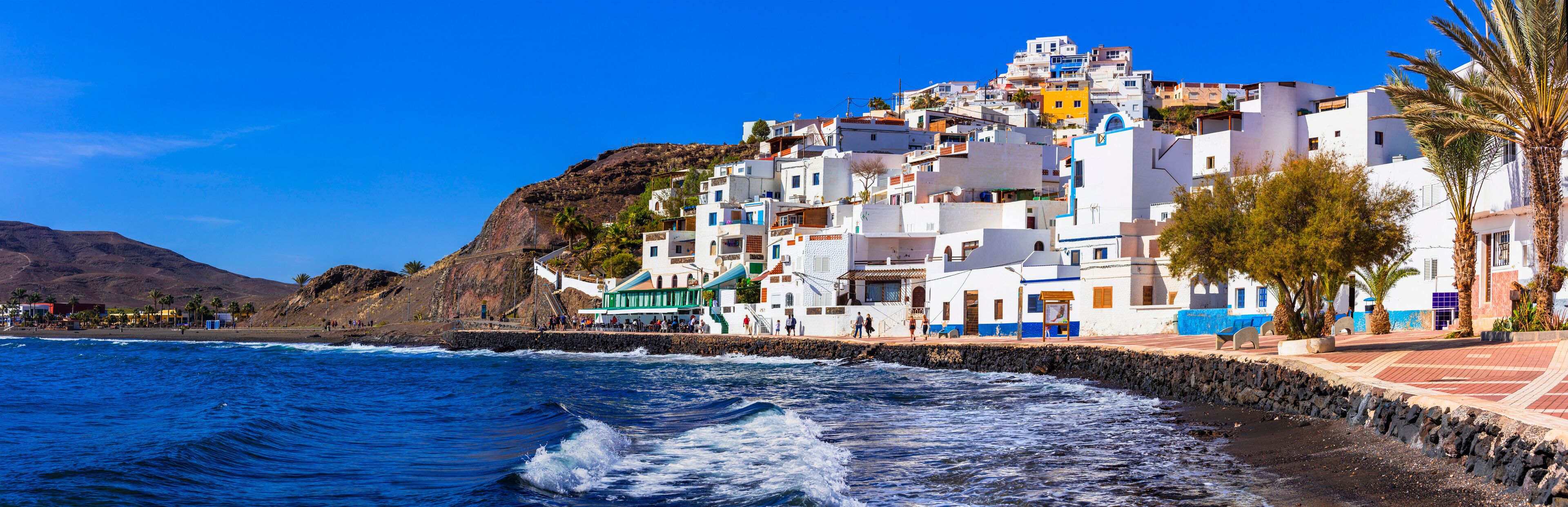 A coastal town with white buildings, a rocky hillside, and the ocean.