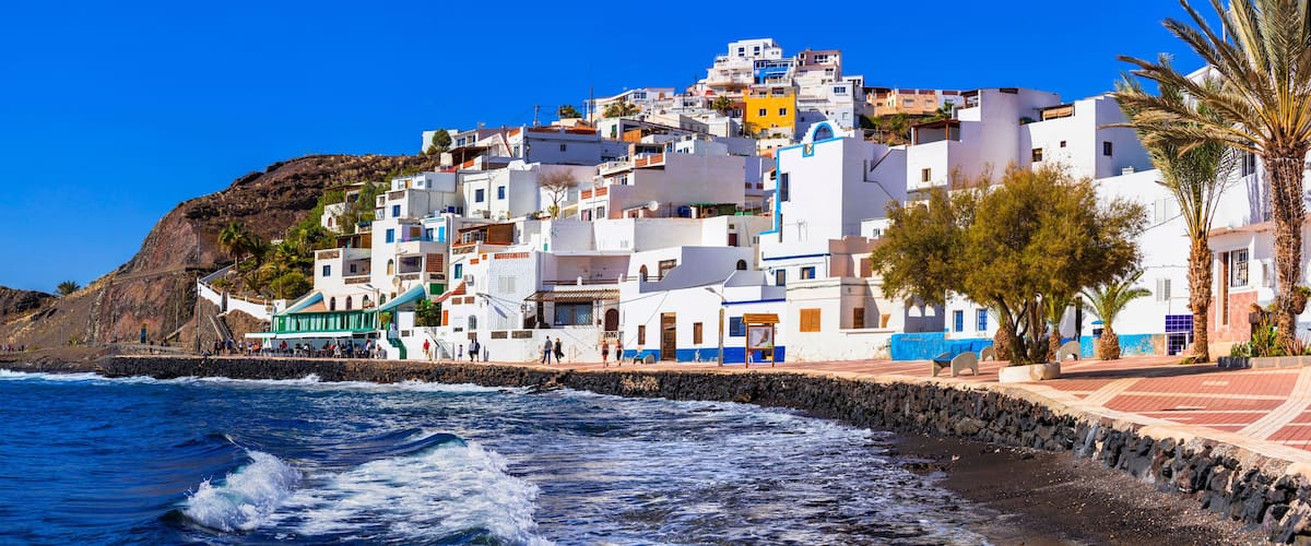 A coastal town with white buildings, a rocky hillside, and the ocean.