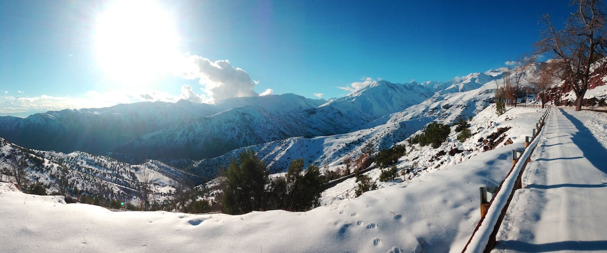 A snow-covered mountain landscape with a clear sky and a sun shining through the clouds.