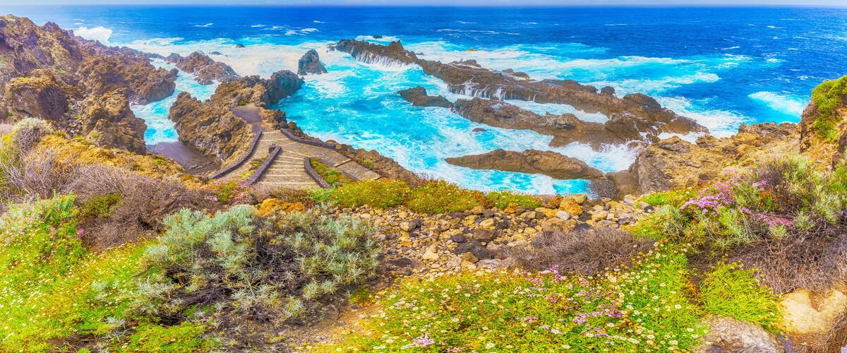 A coastal landscape with rocky cliffs, a sea view, and a stone staircase leading down to the water.