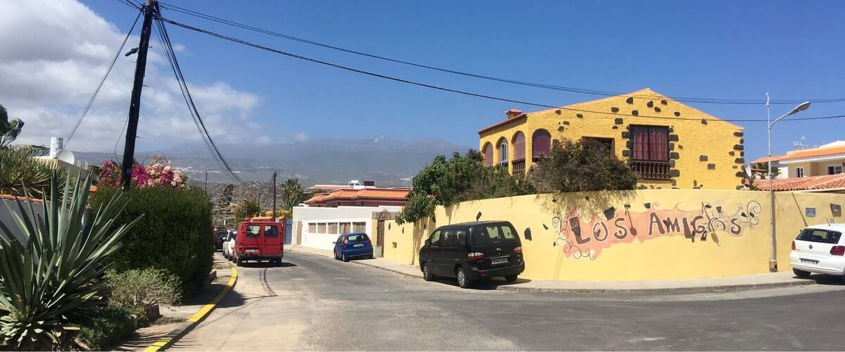 A street with parked cars, a yellow building with a mural, and a red van.