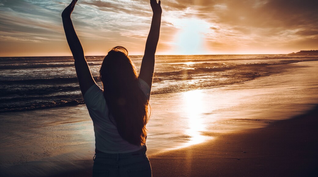 mujer con las manos en alto en la playa atardecer