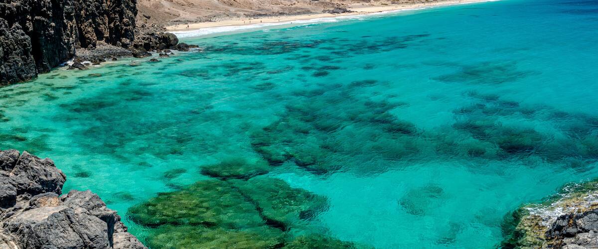 A coastal landscape with clear turquoise waters, rocky cliffs, and a distant mountain range.