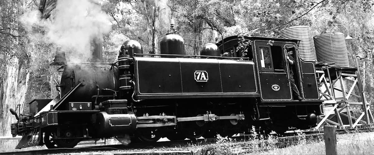 Eine Dampflokomotive mit der Nummer 7A auf Schienen, umgeben von Bäumen.