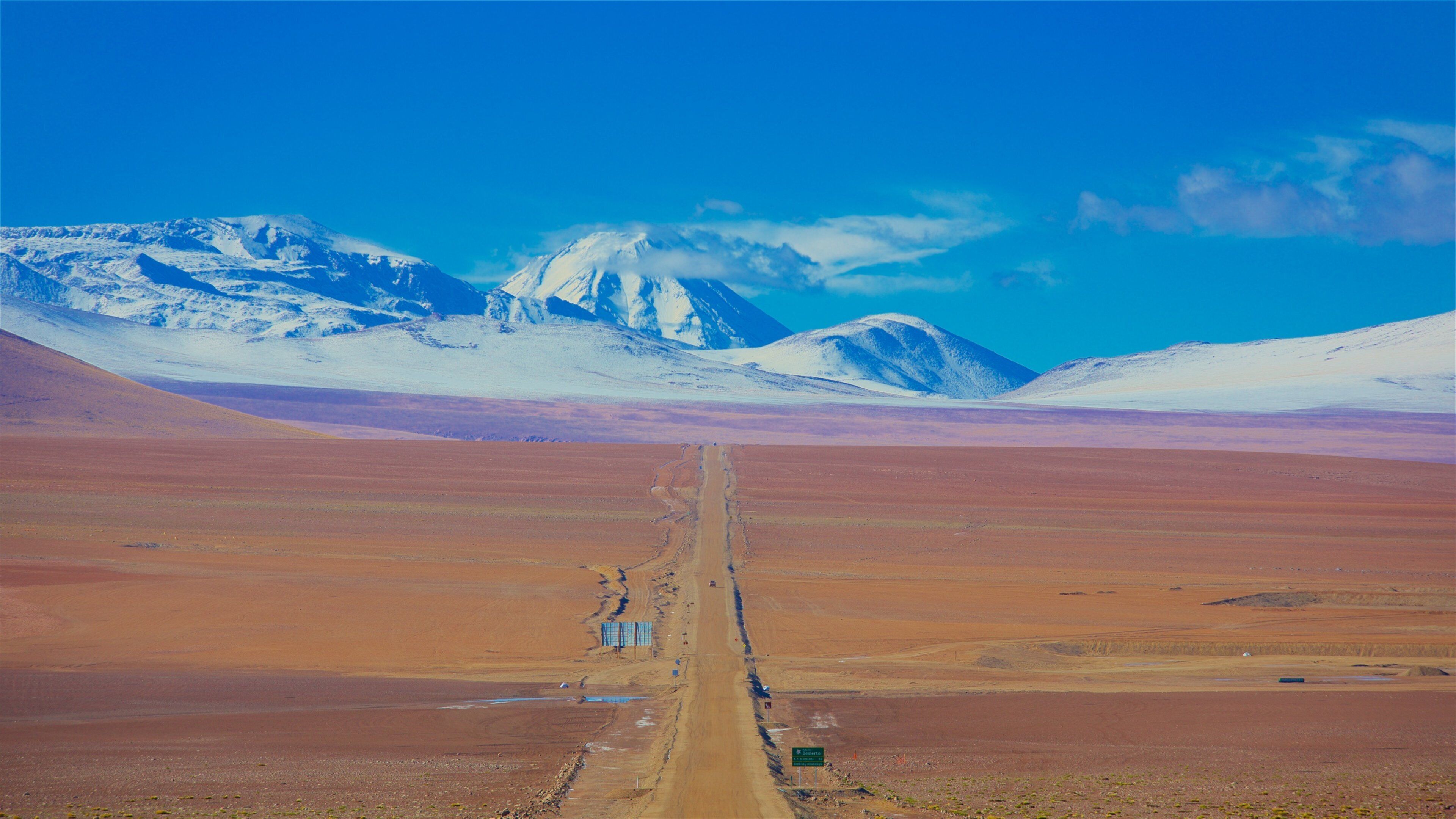 A road leading to snow-capped mountains in a barren landscape.