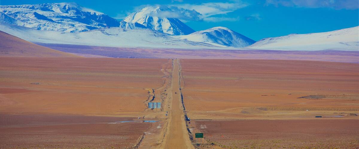 A road leading to snow-capped mountains in a barren landscape.