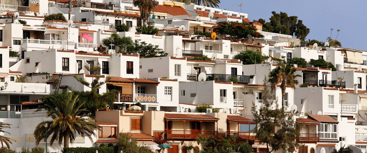 A hillside of white buildings with red-tiled roofs, palm trees, and a clear blue sky.
