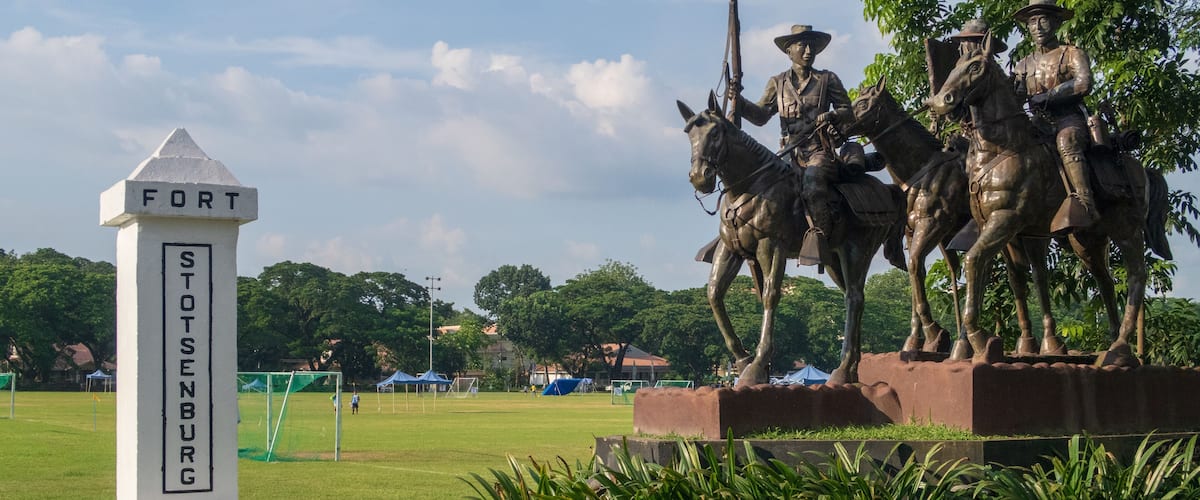 A statue of soldiers on horseback, a monument labeled "FORT STENBURY 1902", and a grassy field with trees in the background.