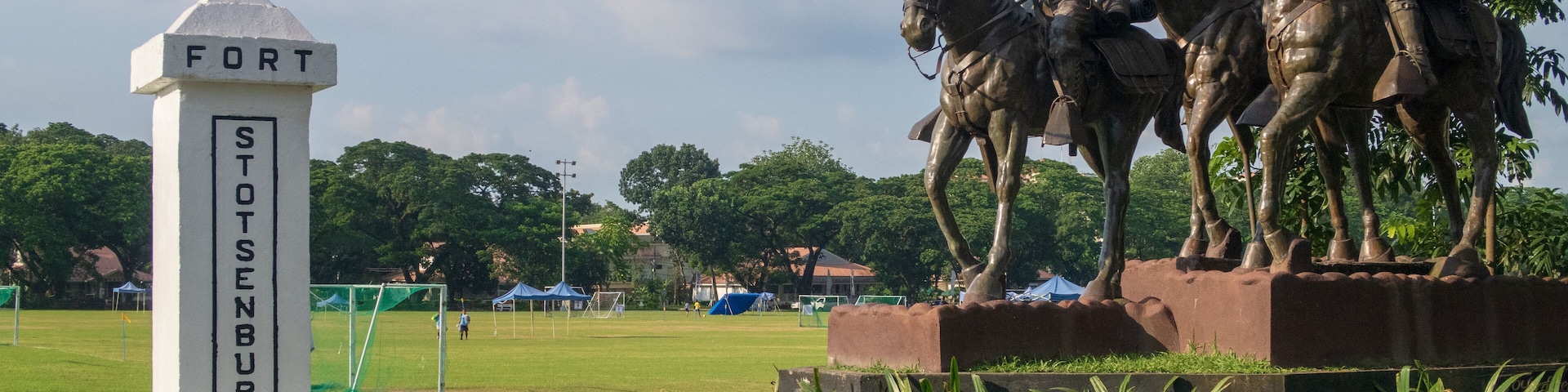 A statue of soldiers on horseback, a monument labeled "FORT STENBURY 1902", and a grassy field with trees in the background.