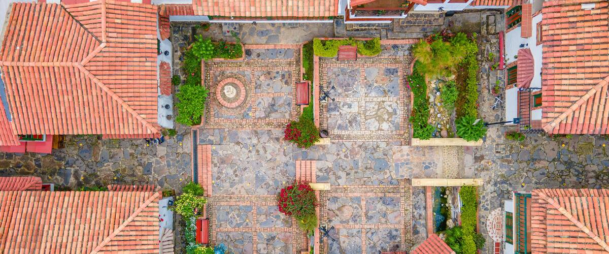 An aerial view of a courtyard with red-tiled roofs, stone pathways, and lush greenery.