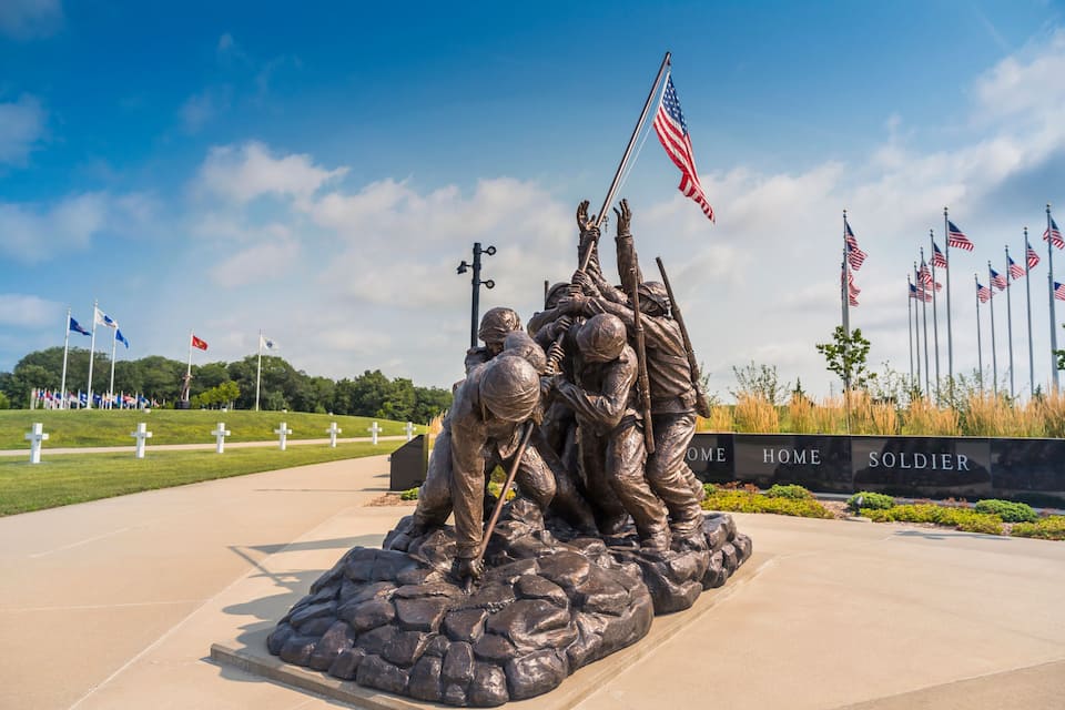 A bronze statue of soldiers raising a flag, surrounded by flags and crosses.