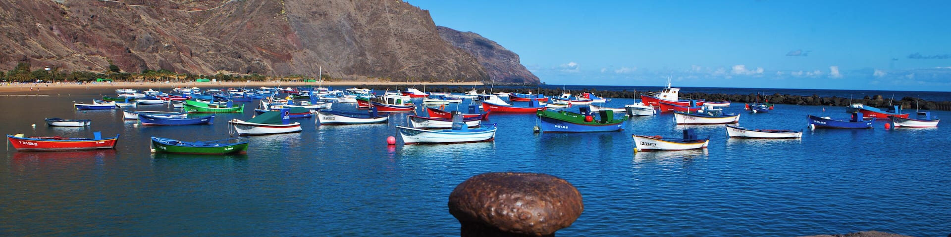 A harbor with numerous colorful boats docked near a rocky coastline.