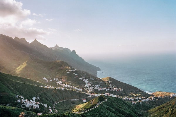 A coastal town nestled in a valley with terraced fields and a winding road leading to the sea.