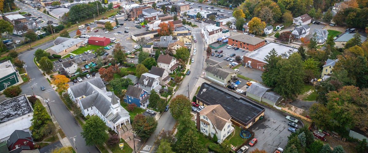 An aerial view of a town with a mix of residential and commercial buildings, surrounded by autumn-colored trees.