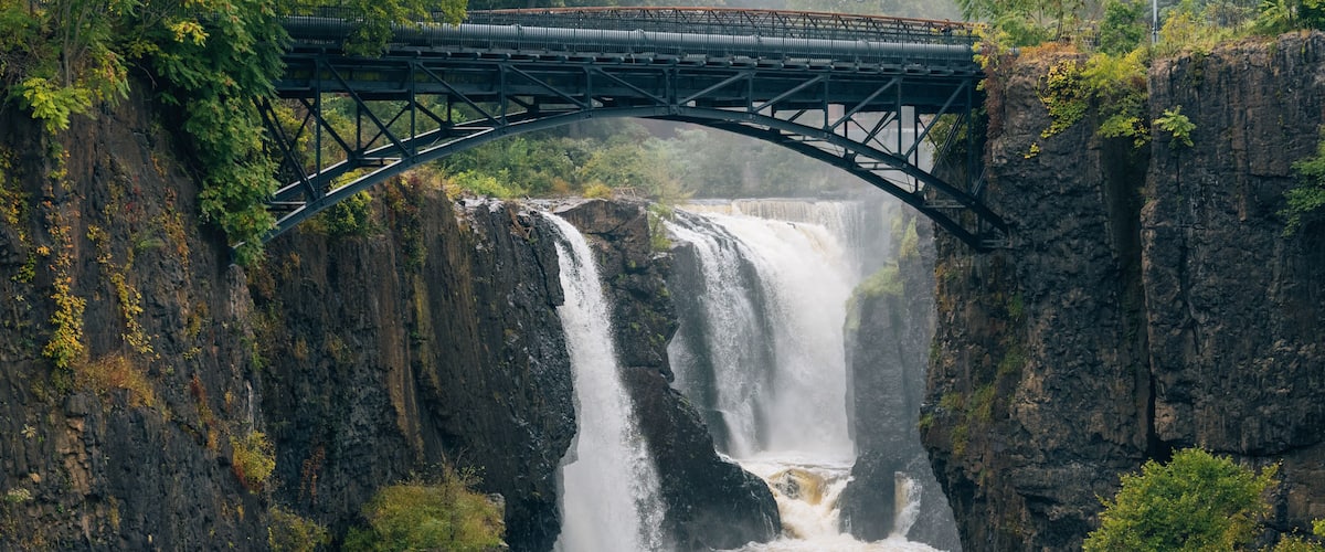 Een brug over een waterval, met aan de zijkant rotswanden en begroeiing.