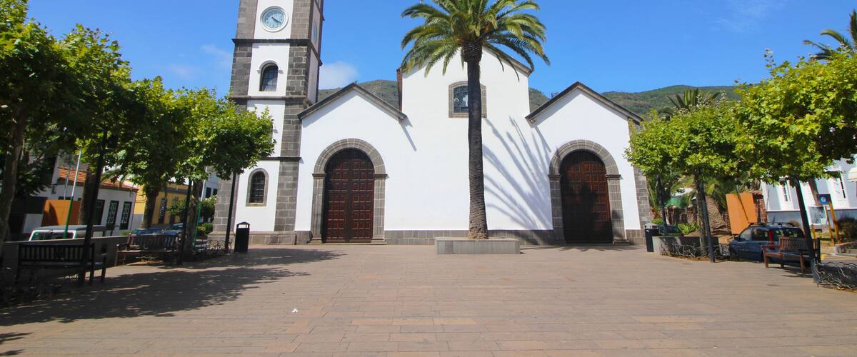 A church with a clock tower, palm trees, and a clear blue sky.