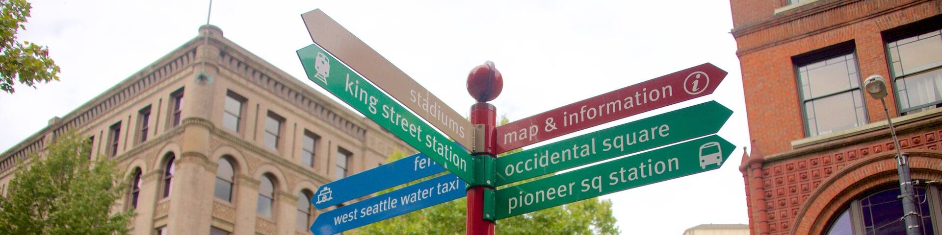 A directional signpost with multiple arrows pointing to various destinations such as 'King Street', 'Stadiums', 'West Seattle Water Taxi', 'Map & Information', 'Occidental Square', and 'Pioneer Sq Station'.