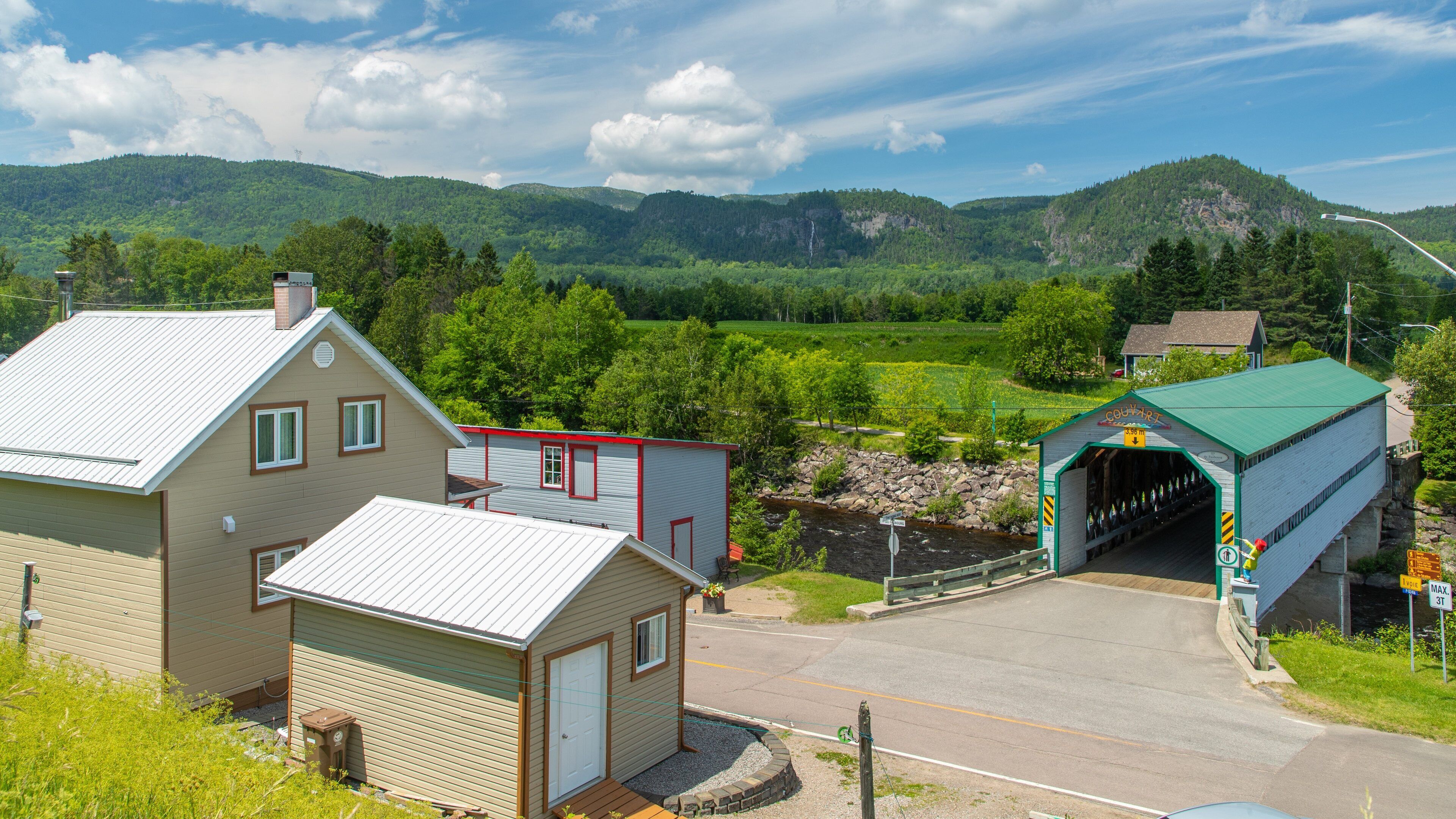 A rural town with a covered bridge, a house, and a mountain backdrop.