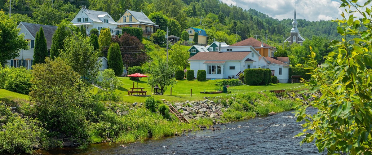 A river flowing through a lush green valley with houses and a church on the hillside.
