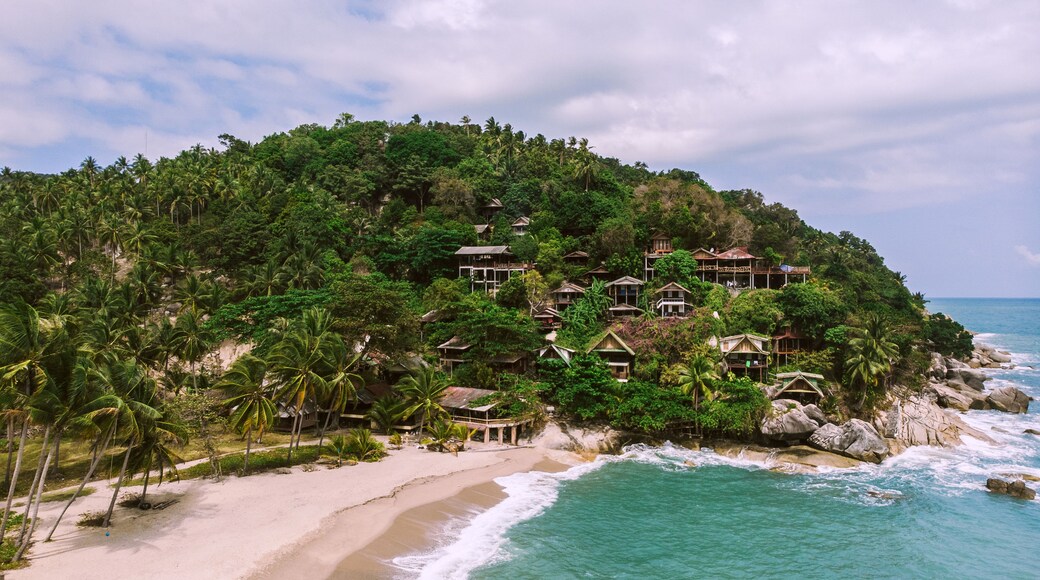 A tropical beach with a resort on a hillside, clear turquoise waters, and a sandy shoreline.