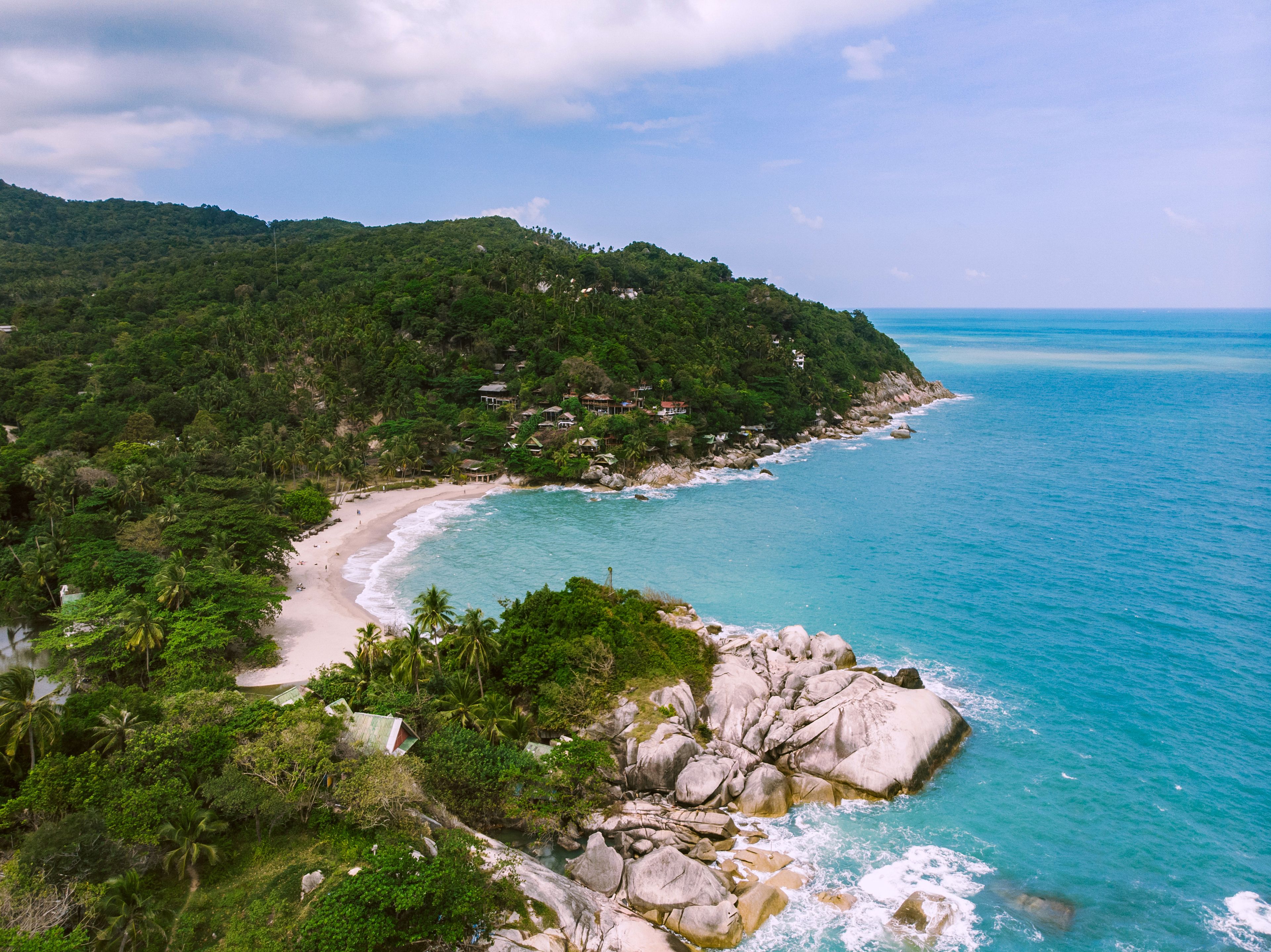 A coastal landscape with a sandy beach, rocky shoreline, and lush green hills.