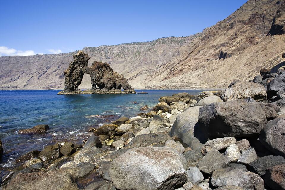 Una costa rocosa con una formación rocosa prominente en forma de arco sobre el agua.