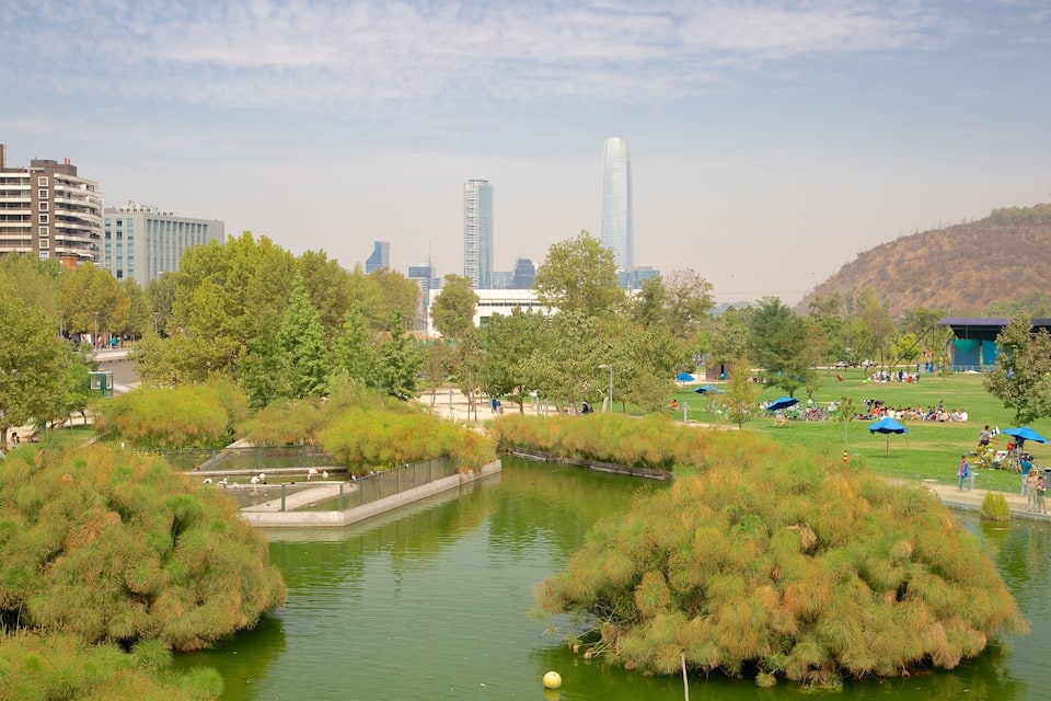 A park with a pond, trees, and a cityscape in the background.