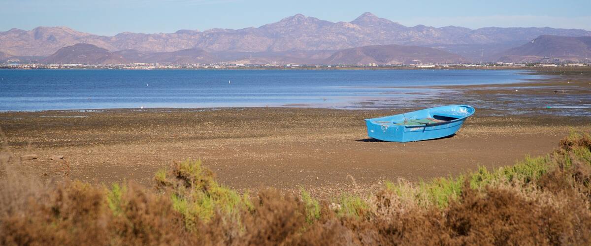A blue boat on a beach with mountains in the background.