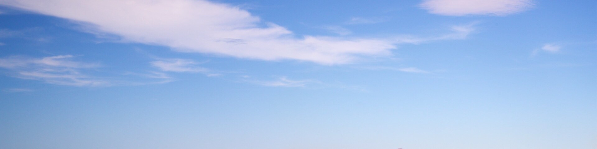 Un paisaje costero con cielo despejado, mar tranquilo y montañas a lo lejos.