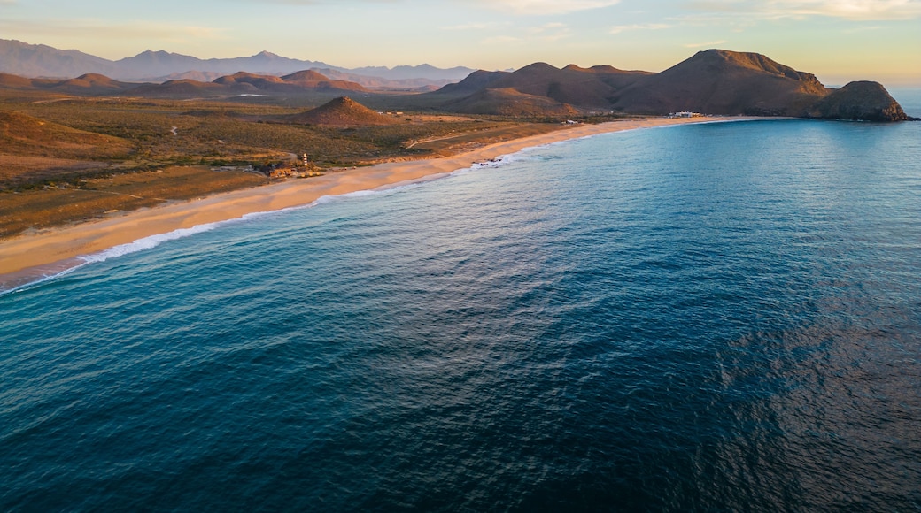 A coastal landscape with a beach, ocean, and distant mountains.