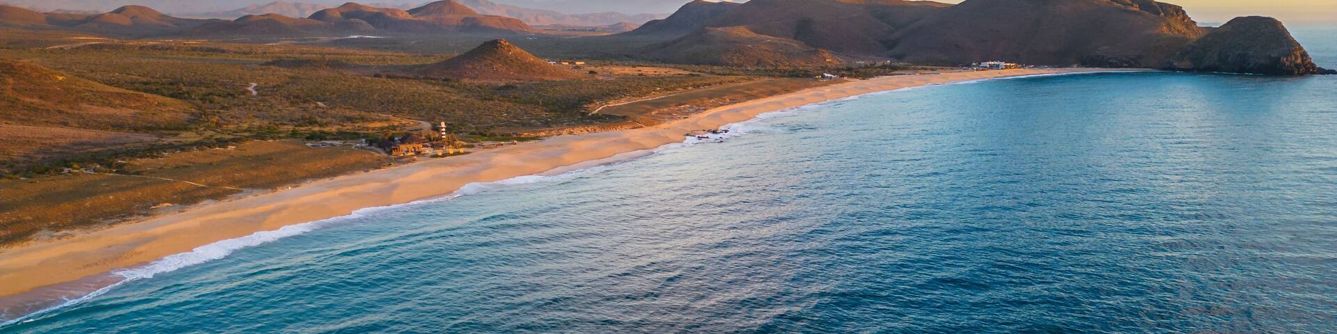 A coastal landscape with a beach, ocean, and distant mountains.