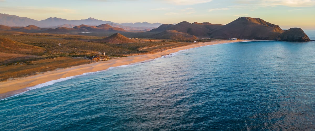 A coastal landscape with a beach, ocean, and distant mountains.
