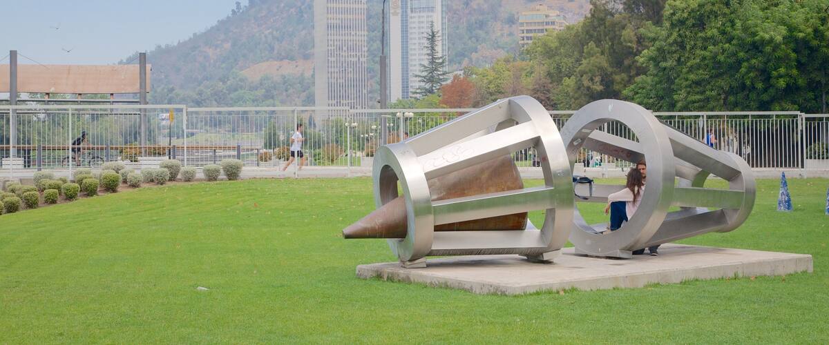 A sculpture in a park with a hilly background and buildings.